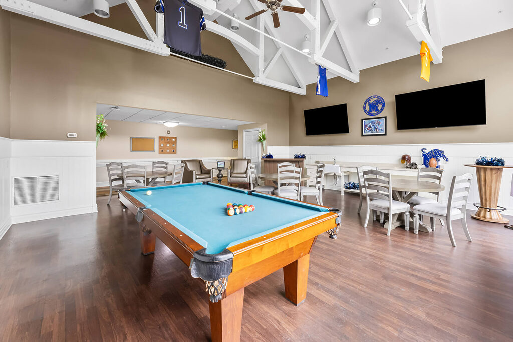 Community game room with a pool table and seating area under vaulted ceiling.