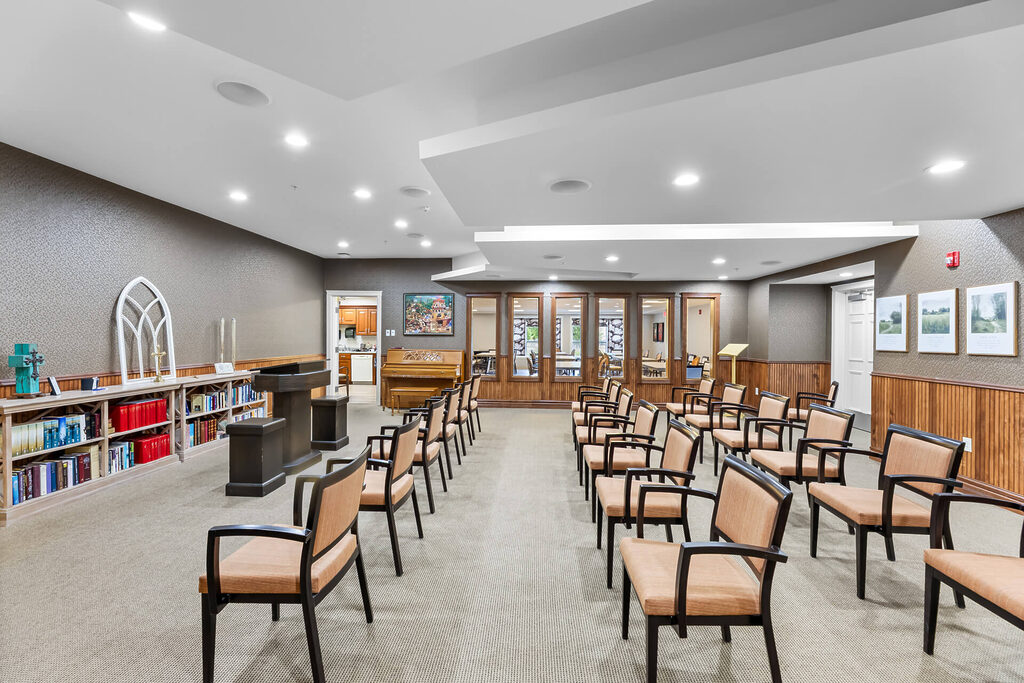 Community room with chairs, a piano, and bookshelves for resident gatherings.
