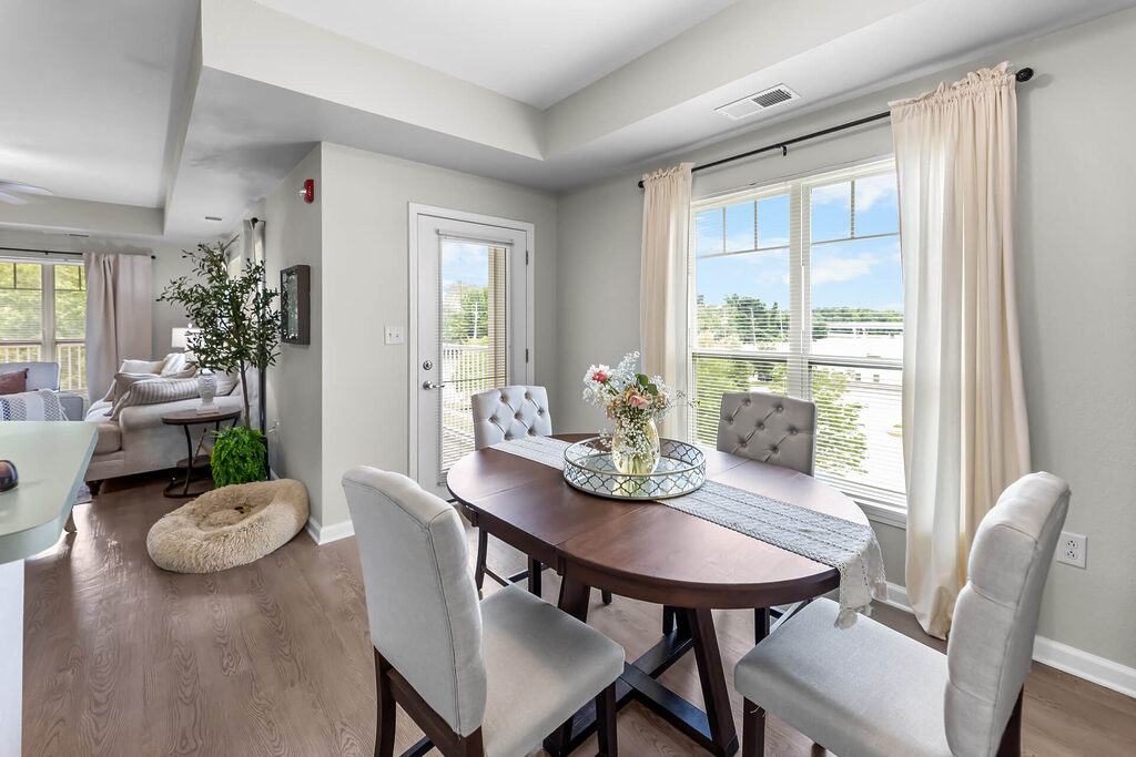 Bright dining area with a table and chairs, near a window with light curtains.